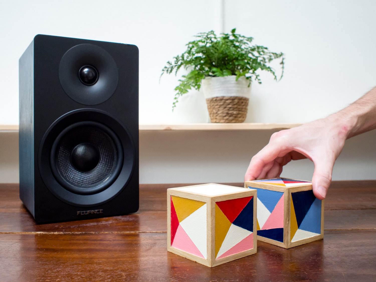 A photo of ml.cubes product prototype on a wooden desk next to a music speaker with a hand reaching out to grab one.