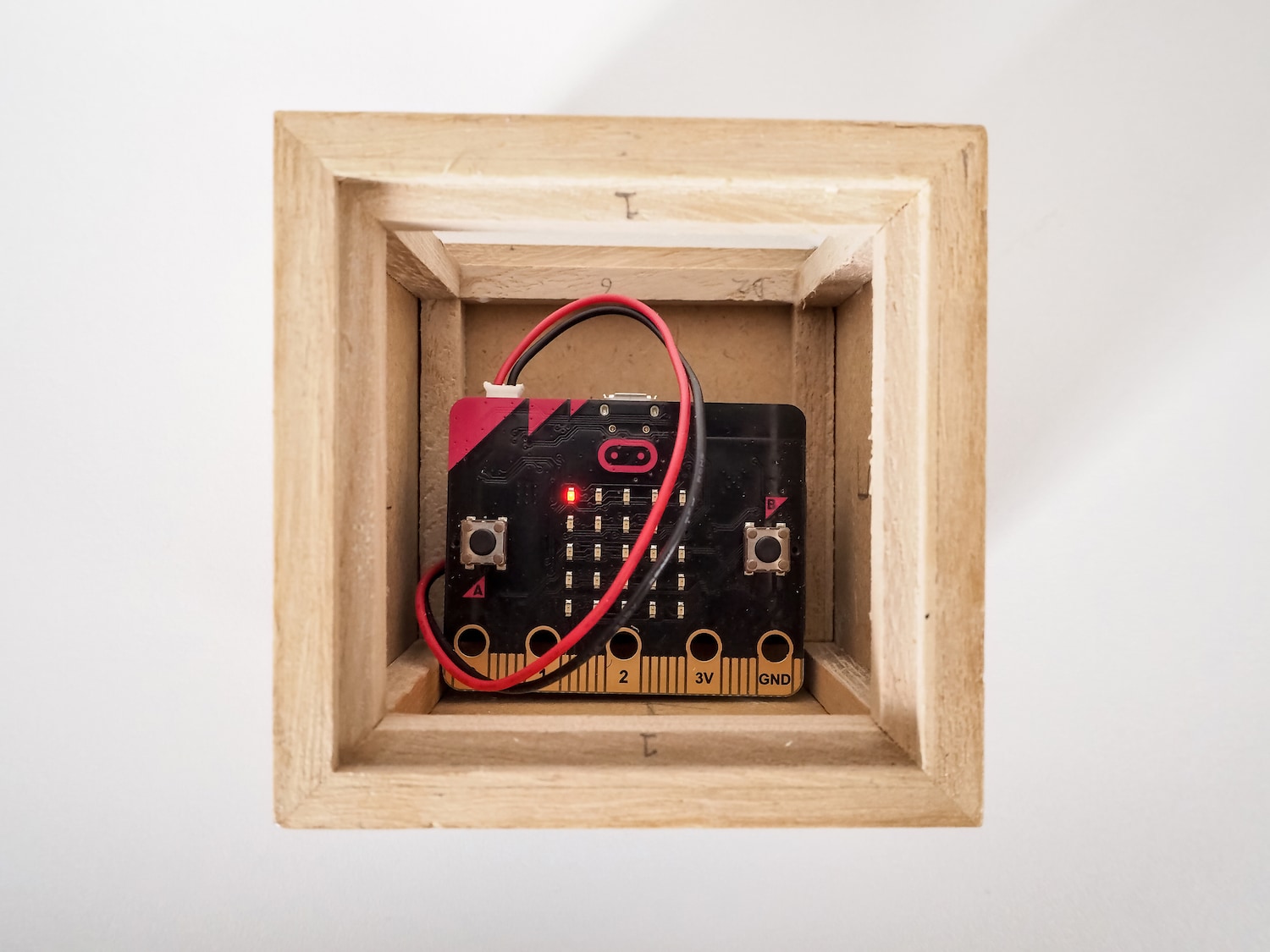 A photo of a micro-computer inside a wooden cube with a solid white background.