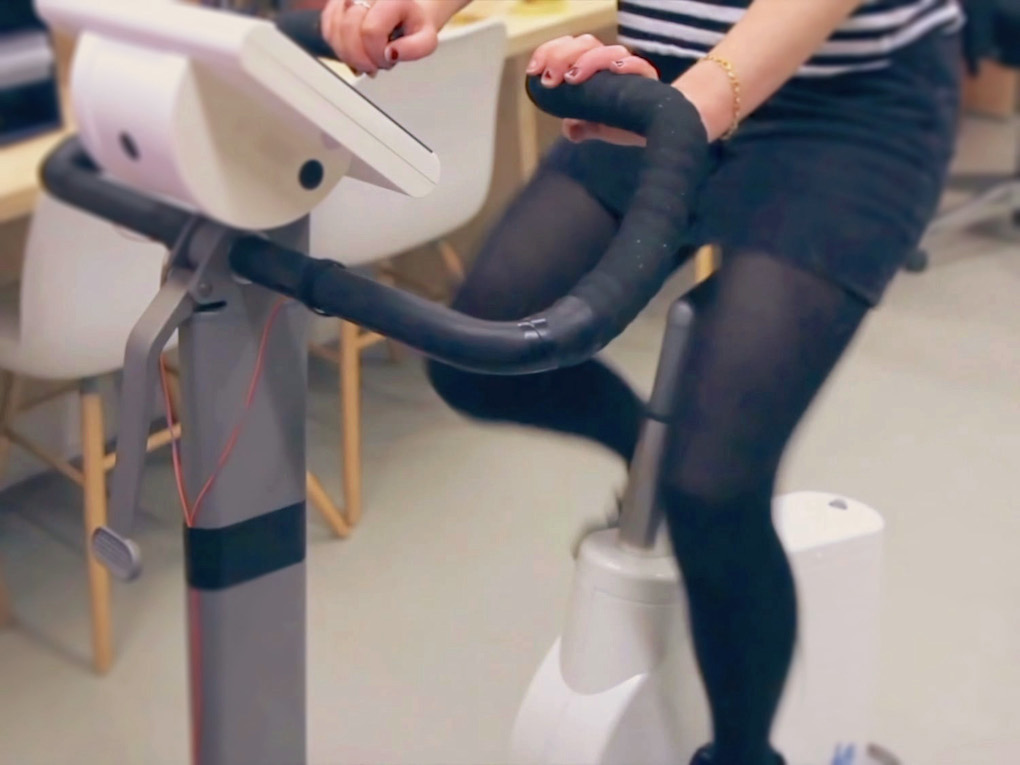 A photo of a woman in a black skirt cycling on an exercise bike.